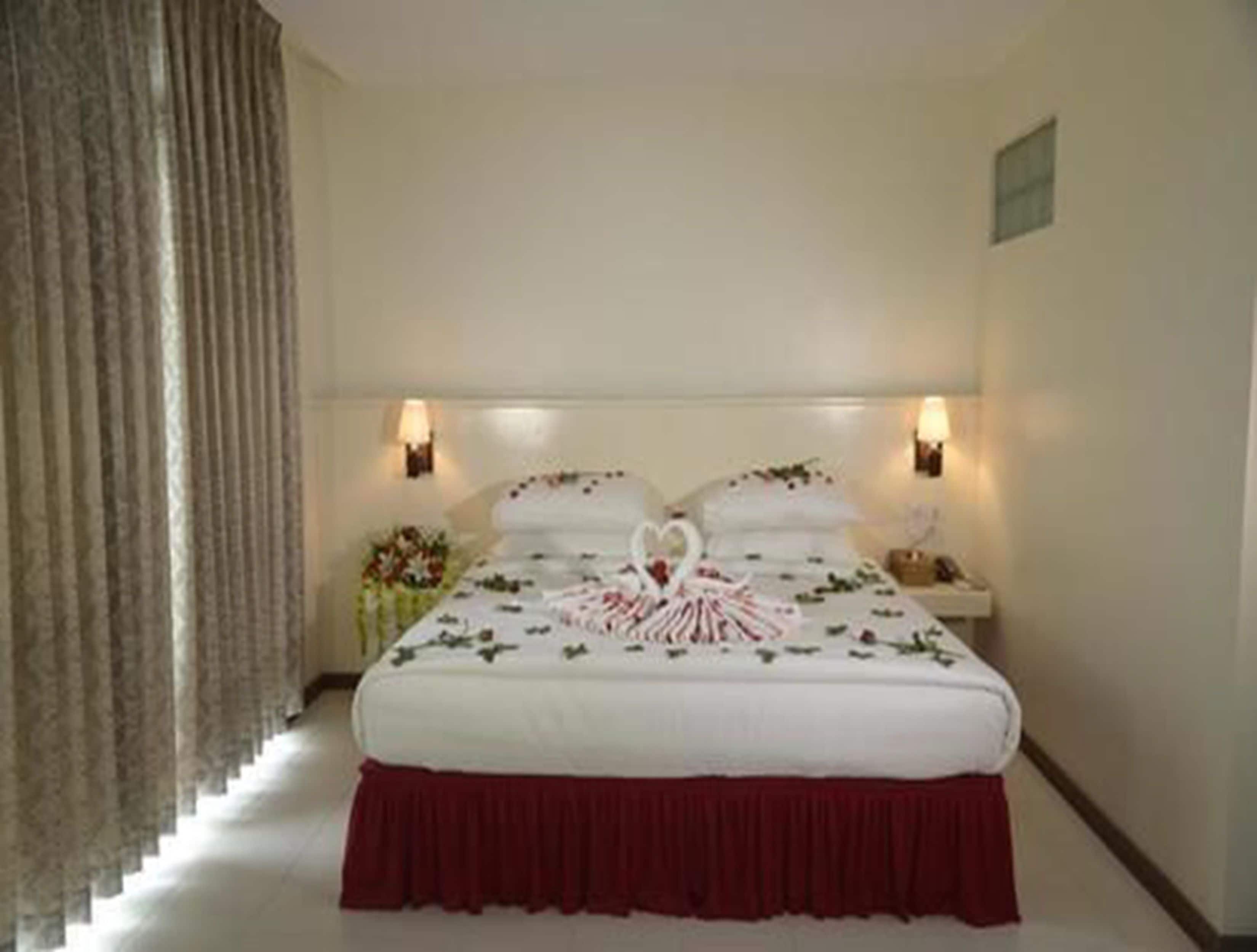 Una habitación de hotel con cama, mesita de noche, lámpara y ventana con cortinas.