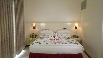 Una habitación de hotel con cama, mesita de noche, lámpara y ventana con cortinas.
