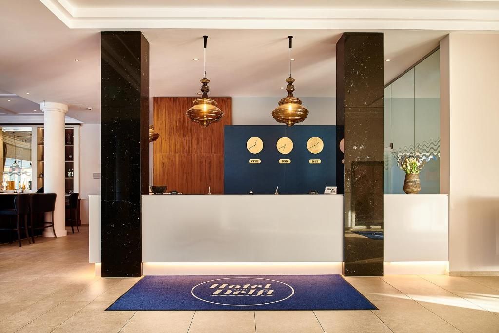 A hotel reception desk with a blue mat, wooden paneling, and three wall clocks.