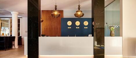 Un mostrador de recepción de hotel con un felpudo azul, paneles de madera y tres relojes de pared.