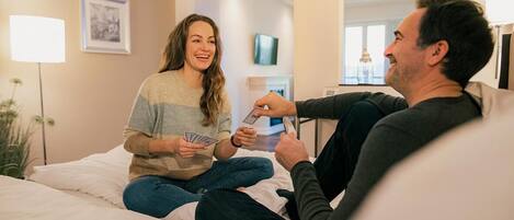 A couple sitting on a bed in a hotel room, playing cards.
