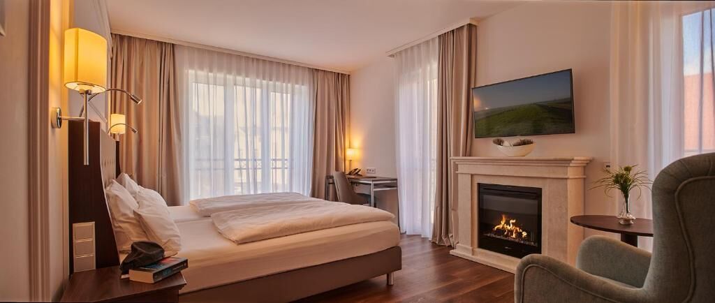 Quarto de hotel com cama, televisão sobre a lareira e uma escrivaninha com cadeira.