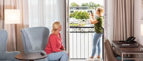 Habitación de hotel con balcón, zona de estar con una mesa y escritorio con teléfono.