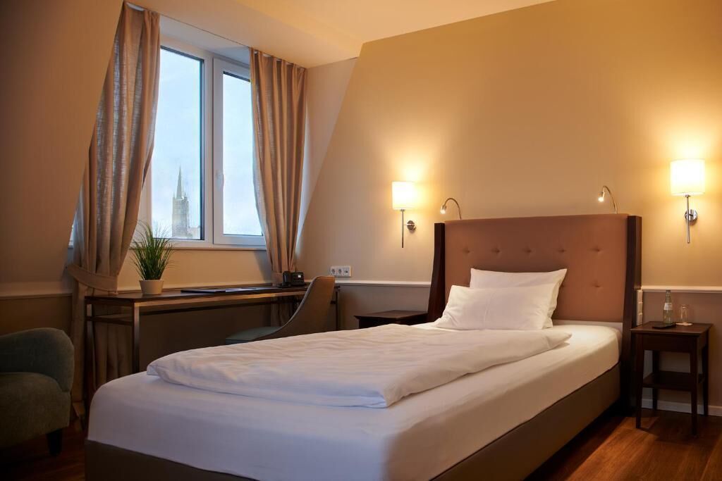 A hotel room with a large bed, a desk, a chair, and a window with curtains.