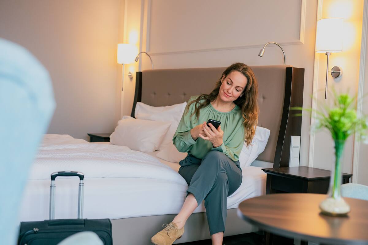A hotel room with a bed, a bedside table, a lamp, and a suitcase.