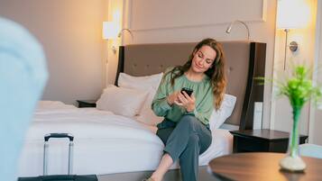 A hotel room with a bed, a bedside table, a lamp, and a suitcase.
