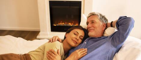 Una pareja recostada en una cama en una habitación con chimenea.
