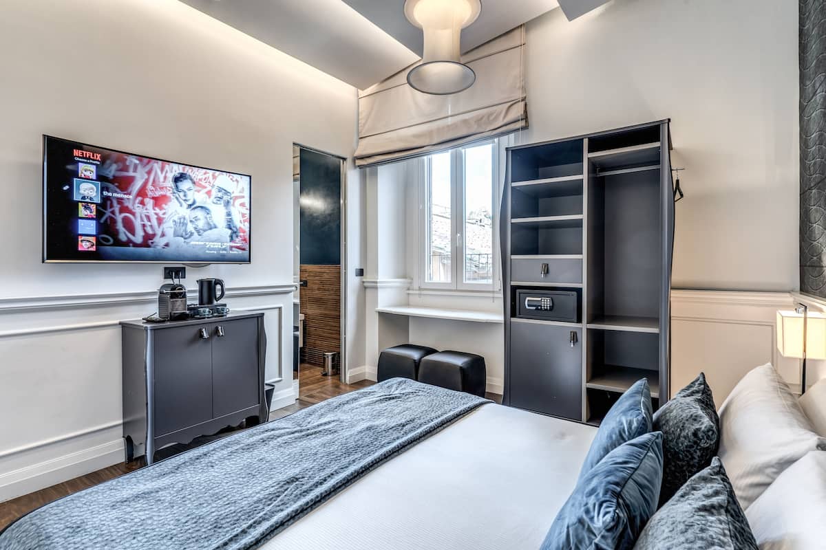 A modern hotel room with a large bed, a TV mounted on the wall, a wardrobe, and a window with a view.