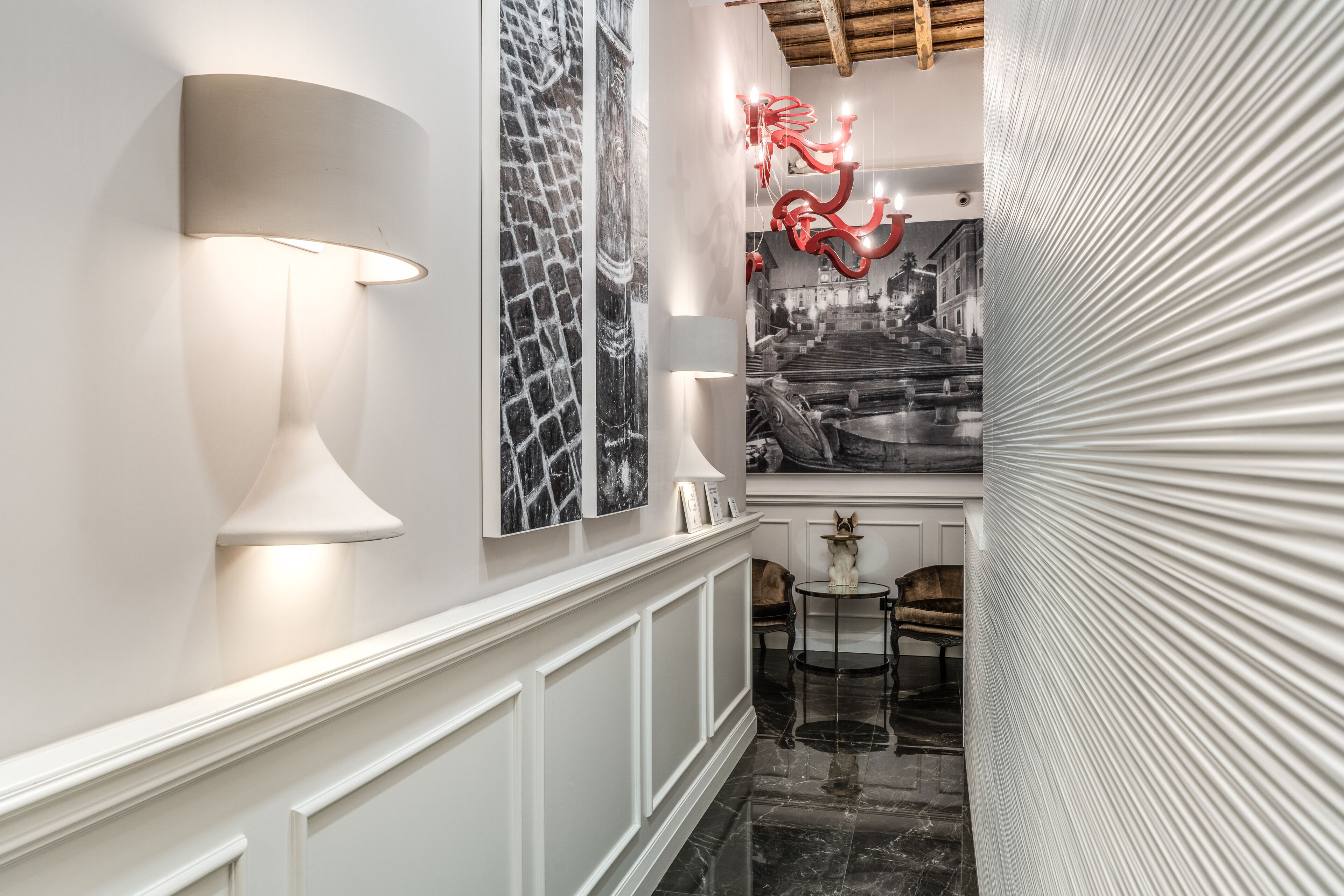 Un couloir avec un mur blanc, une photographie en noir et blanc, une sculpture rouge et une lampe.