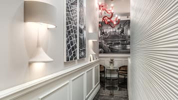 Un couloir avec un mur blanc, une photographie en noir et blanc, une sculpture rouge et une lampe.