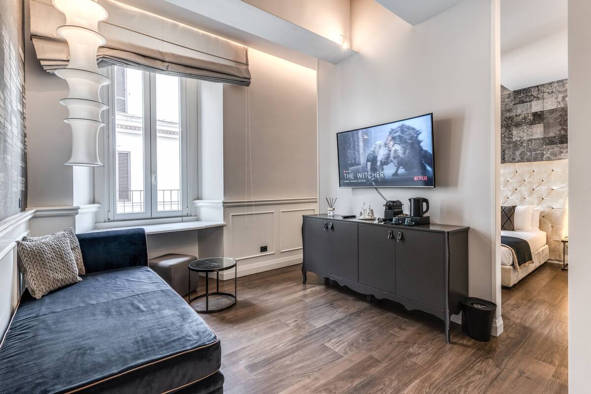 A modern living room with a dark sofa, a small round table, a grey cabinet, and a television displaying 'The Witcher' on Netflix.