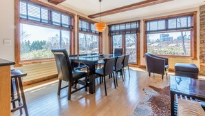 A dining area with a glass table and chairs, large windows with blinds, and a stone wall. - Yukimi 1 (Kutchan)