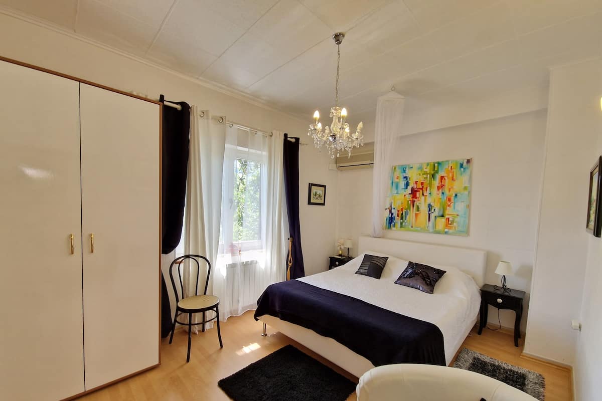 A bedroom with a large bed, a chair, a desk, and a painting on the wall.