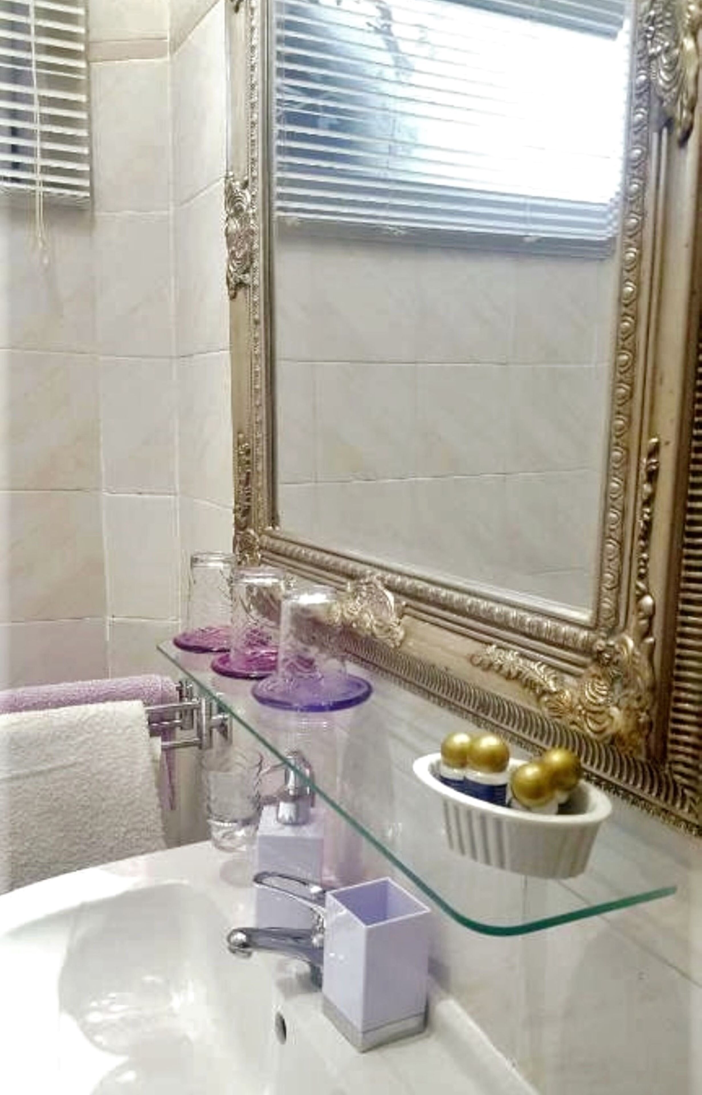 A bathroom with a white sink, a glass shelf with decorative items, and a large ornate mirror.
