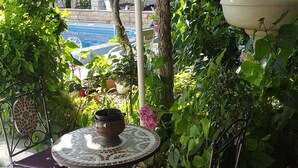 Un patio con una mesa redonda y sillas, rodeado de vegetación y vistas a una piscina.