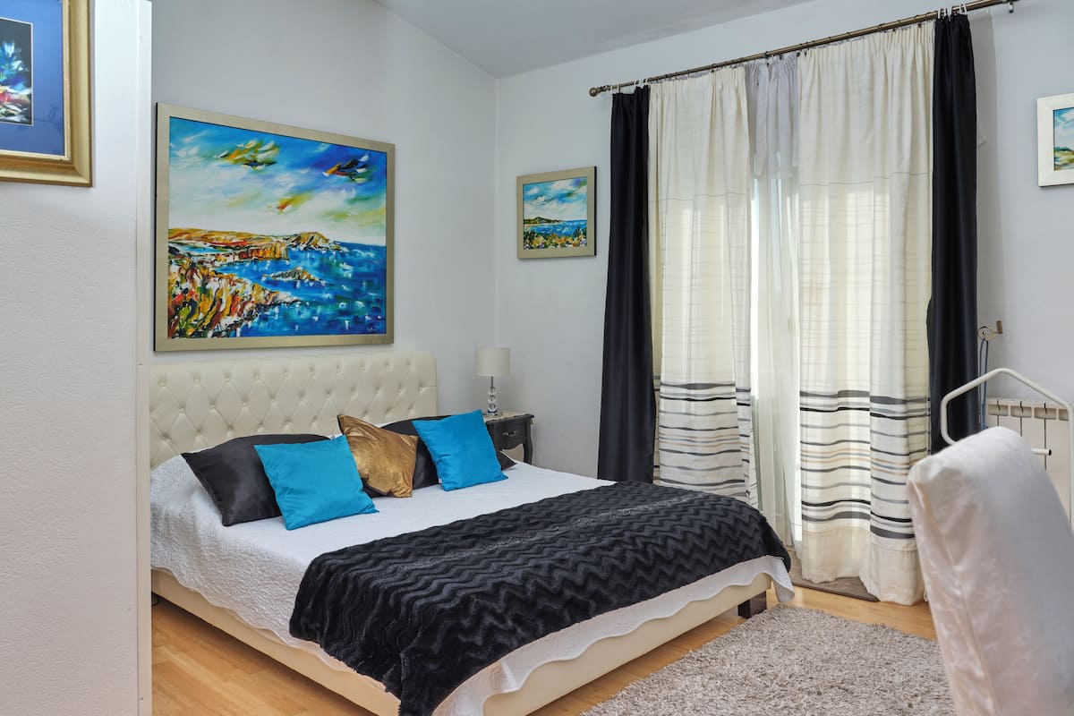 A bedroom with a large bed, a nightstand, a lamp, and two paintings on the wall.