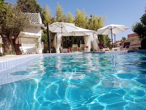 Una piscina azul cristalina con sombrillas y sillas de descanso blancas.
