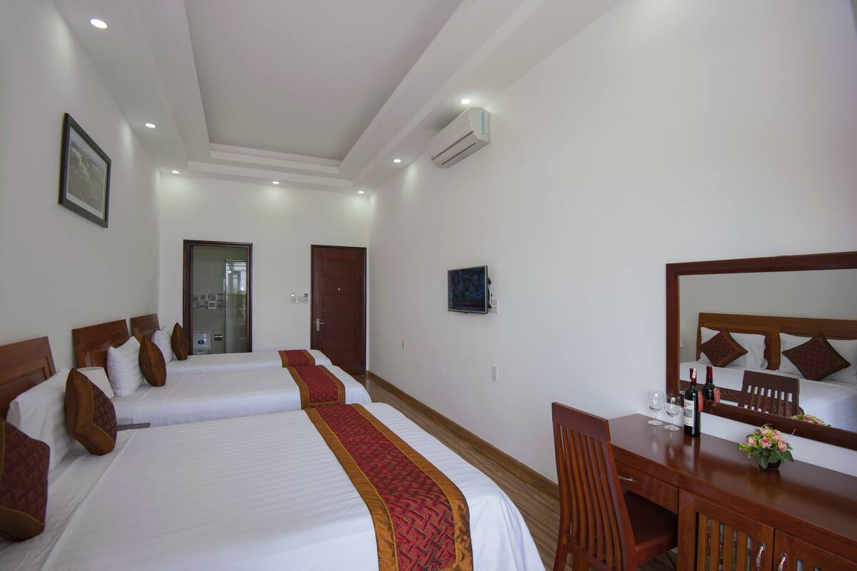 A hotel room with two beds, a wooden desk, a chair, a mirror, and a small table with a vase.