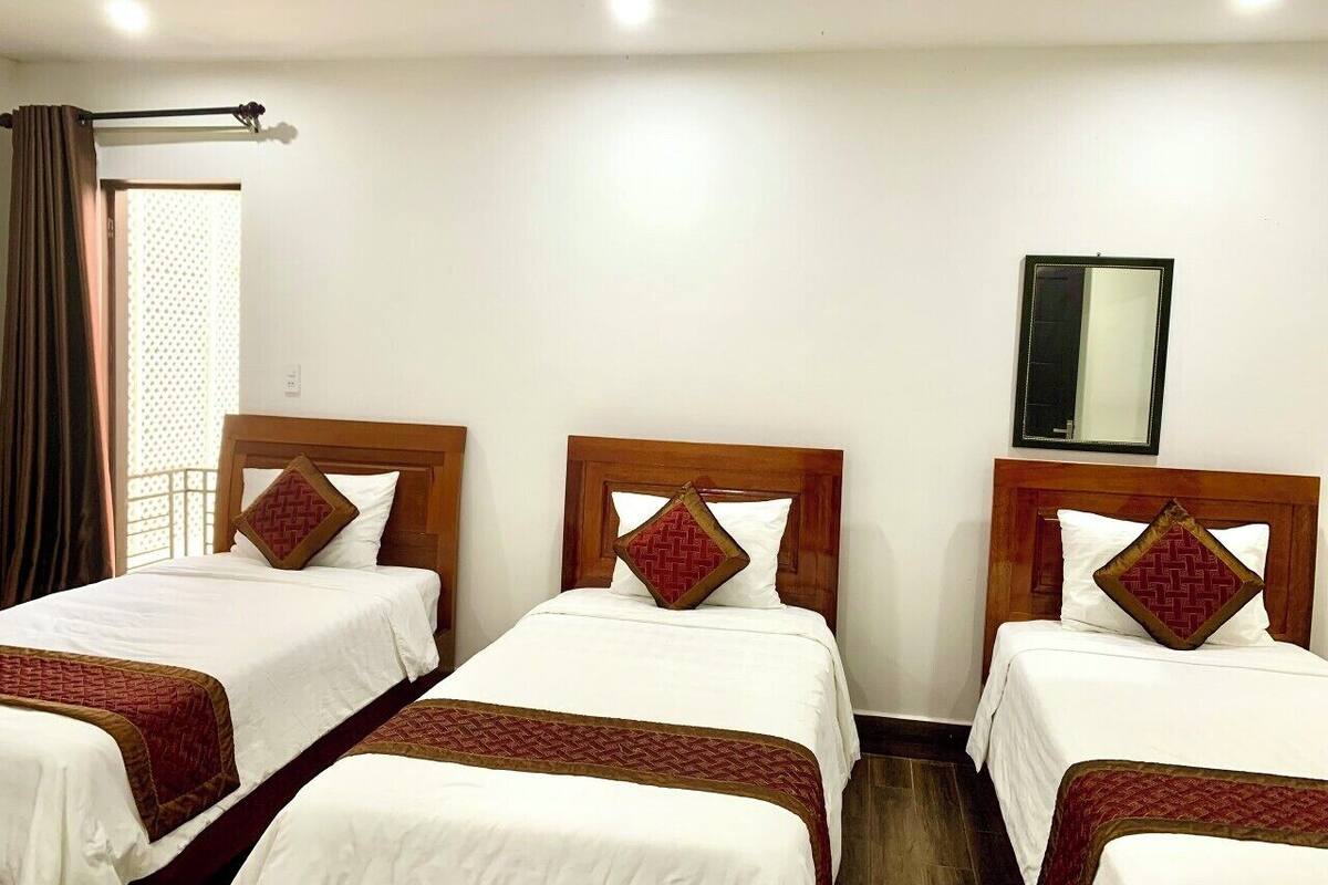 A hotel room with three single beds, each with a wooden headboard and white bedding.