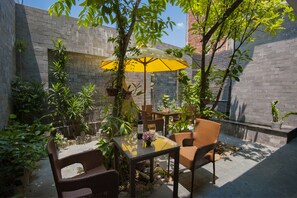 An outdoor patio with wicker furniture, a yellow umbrella, and potted plants. - Hoi An SunLake Villa (Da Nang)