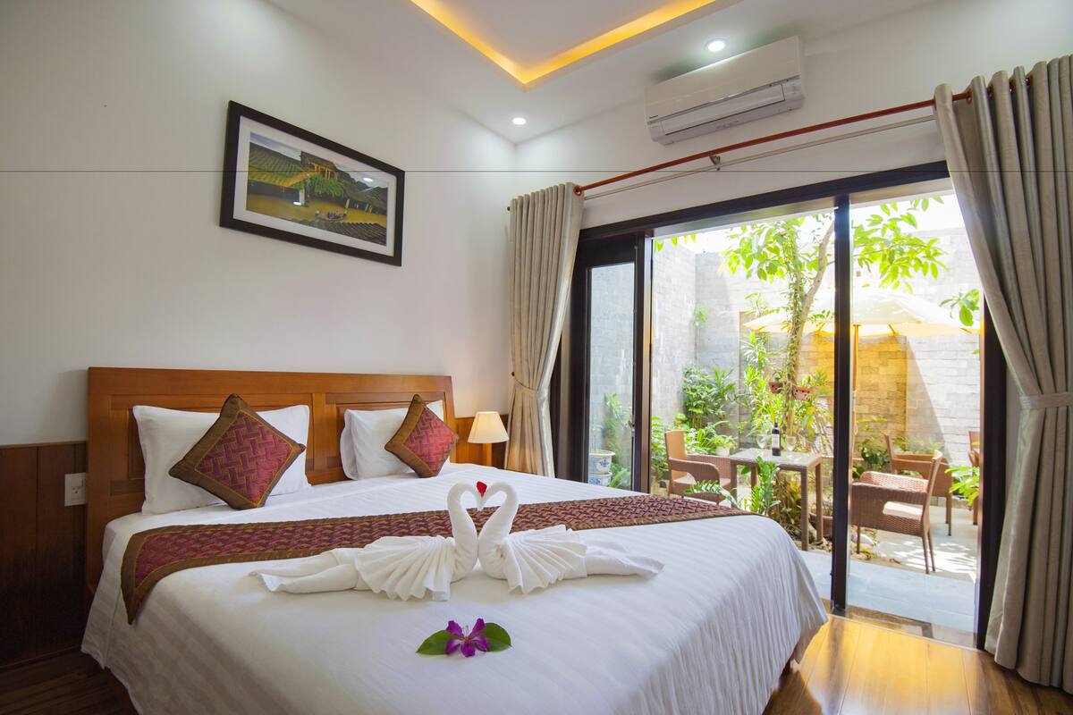 A hotel room with a large bed, a picture on the wall, and a view of the outdoors through a glass door.