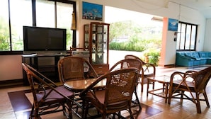 Una sala de estar con televisor, mesa de comedor, sillas de mimbre y un sofá azul.