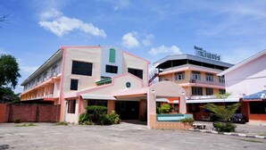 Un hotel de varios pisos con una entrada central, un estacionamiento techado y un letrero con el nombre del hotel.