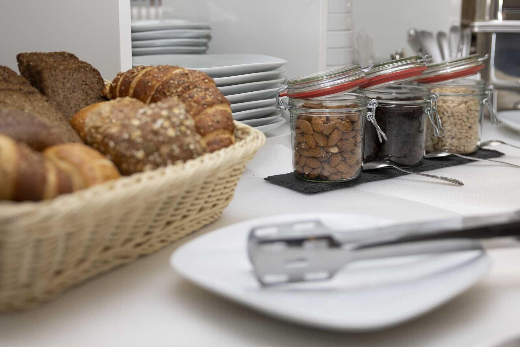 A breakfast buffet with bread, pastries, and jars of nuts.