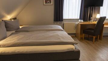 A hotel room with two beds, a desk with a chair, a radiator, and a picture on the wall.