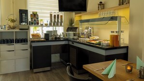 A modern kitchen with a coffee station, buffet setup, and a flat-screen TV. - Hotel Rendsburg (Rendsburg)