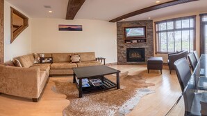 Un salón acogedor con chimenea de piedra, un televisor grande montado encima y un sofá de cuero, junto con una mesa de comedor de vidrio.
