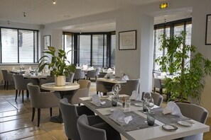 A modern dining area with round tables, grey chairs, and potted plants.
