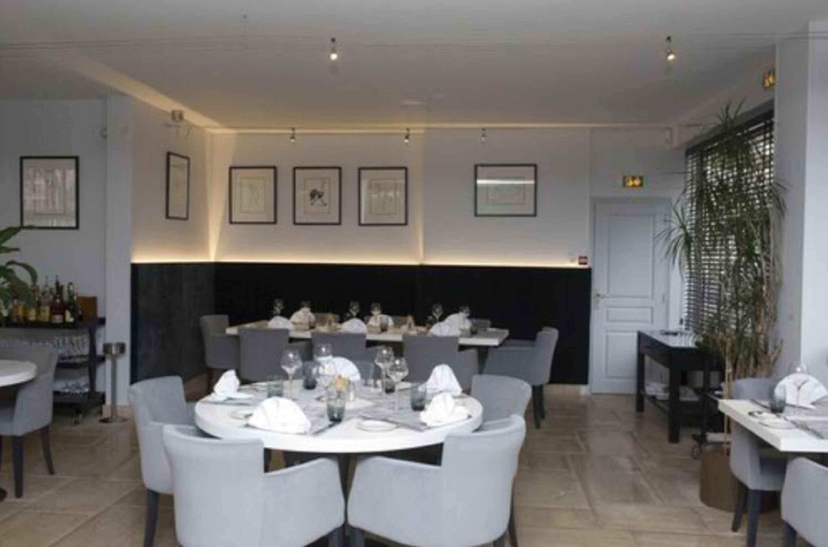 A restaurant with round tables, grey chairs, framed artwork on the walls, and a black partition.
