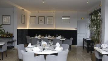 A restaurant with round tables, grey chairs, framed artwork on the walls, and a black partition.