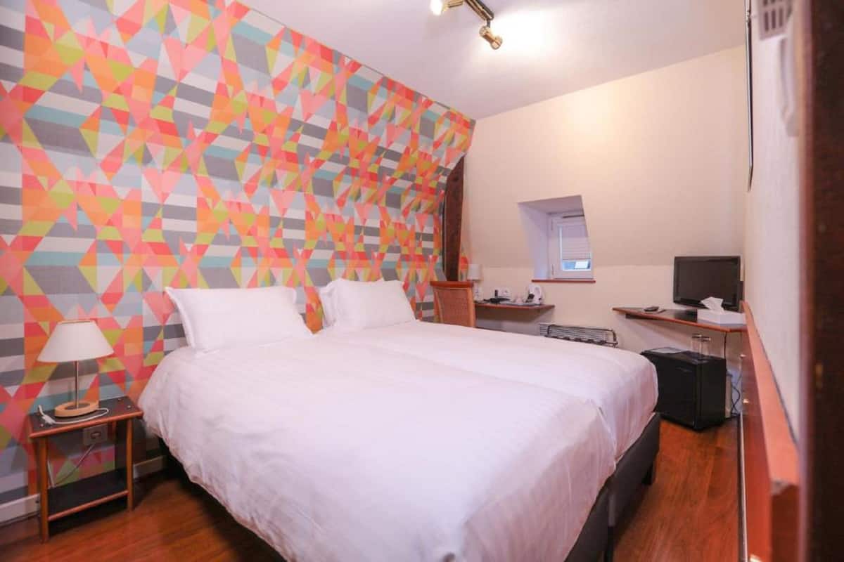 Ein Hotelzimmer mit einem großen Bett, einem Schreibtisch mit Computer und einer Wand mit einem farbenfrohen geometrischen Muster.