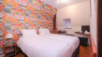 A hotel room with a large bed, a desk with a computer, and a colorful geometric-patterned wall.