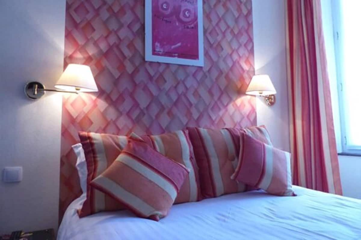 Ein Hotelzimmer mit einem Bett, zwei Wandleuchten, einer Wand mit Muster und einem Fenster mit Vorhängen.