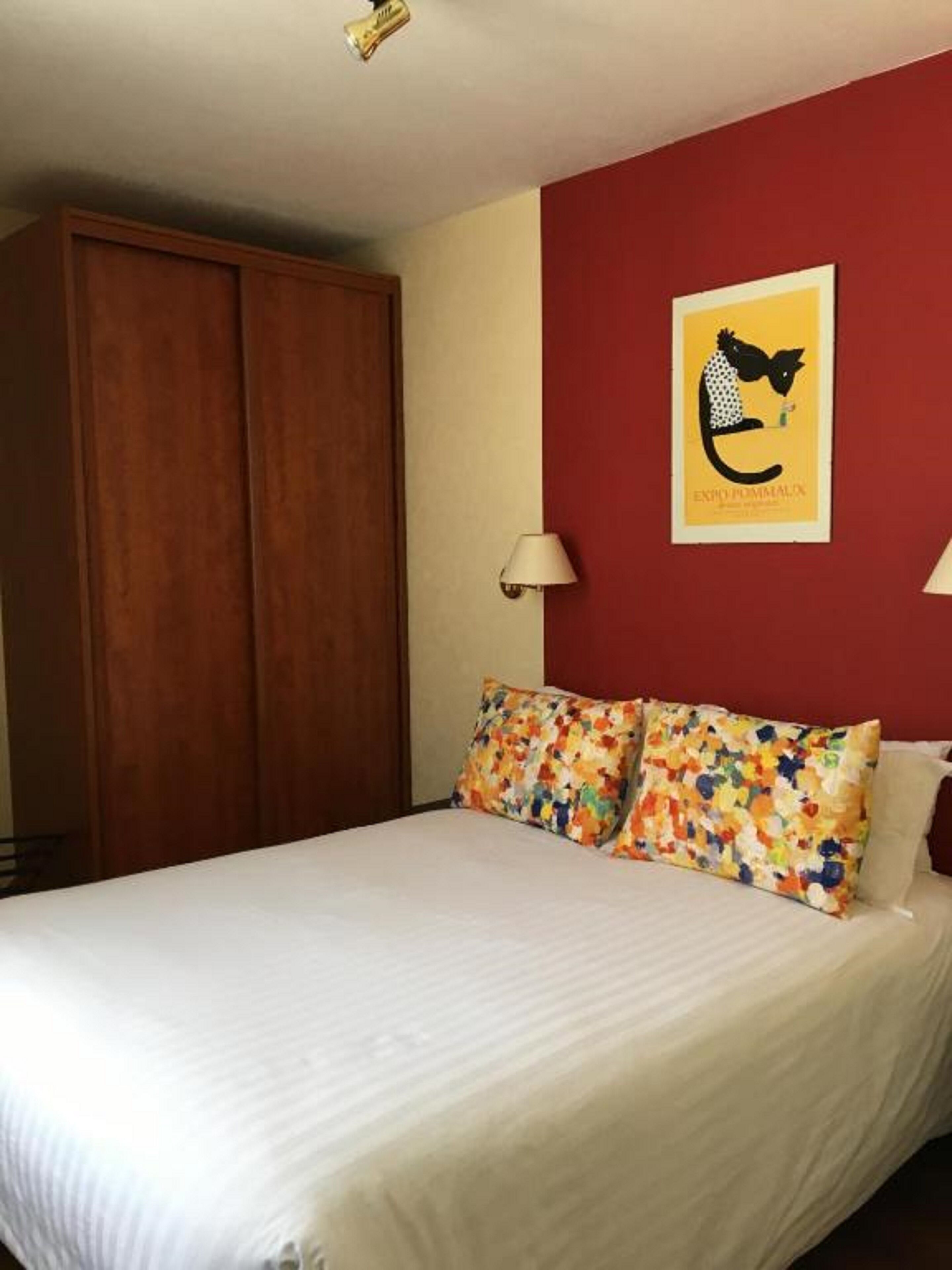 A bedroom with a bed, a red wall, a poster, and a wardrobe.