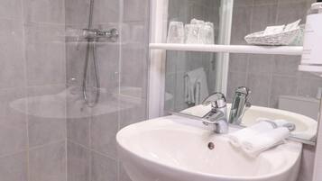 A bathroom with a white sink, a mirror, a shower, and a shelf with toiletries.