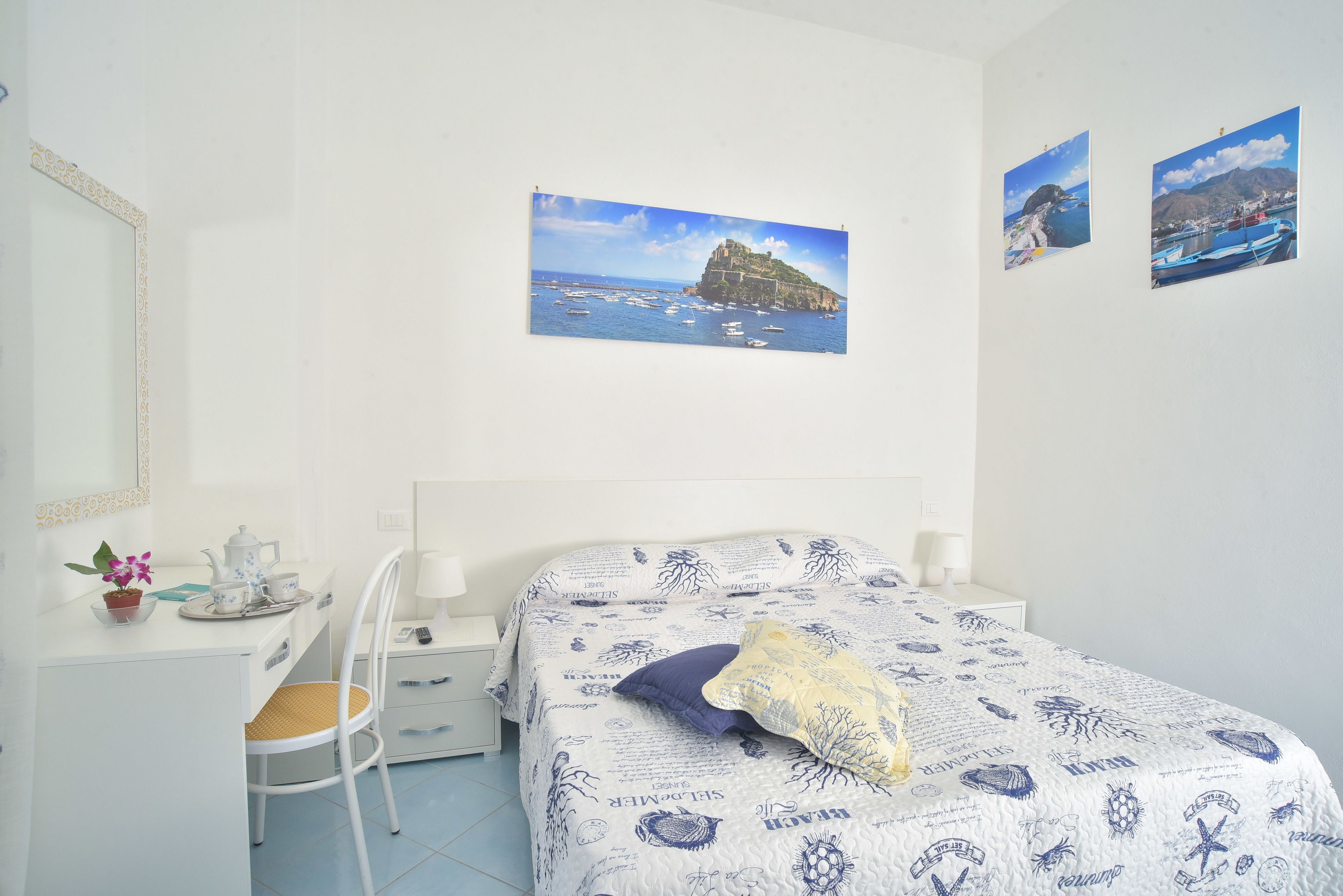 A bedroom with a bed, a desk, a chair, and a mirror. There are two framed pictures on the wall.