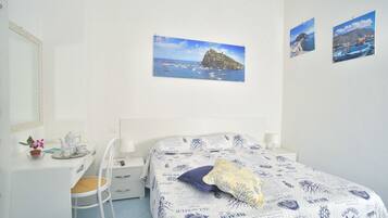A bedroom with a bed, a desk, a chair, and a mirror. There are two framed pictures on the wall.