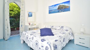 Ein Schlafzimmer mit Bett, Schreibtisch, Stuhl, Nachttisch und einem Fenster mit Vorhängen.