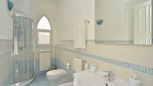 Ein Badezimmer mit Duschkabine aus Glas, Toilette, Waschbecken mit Spiegel und Fenster mit dekorativer Glasverkleidung.