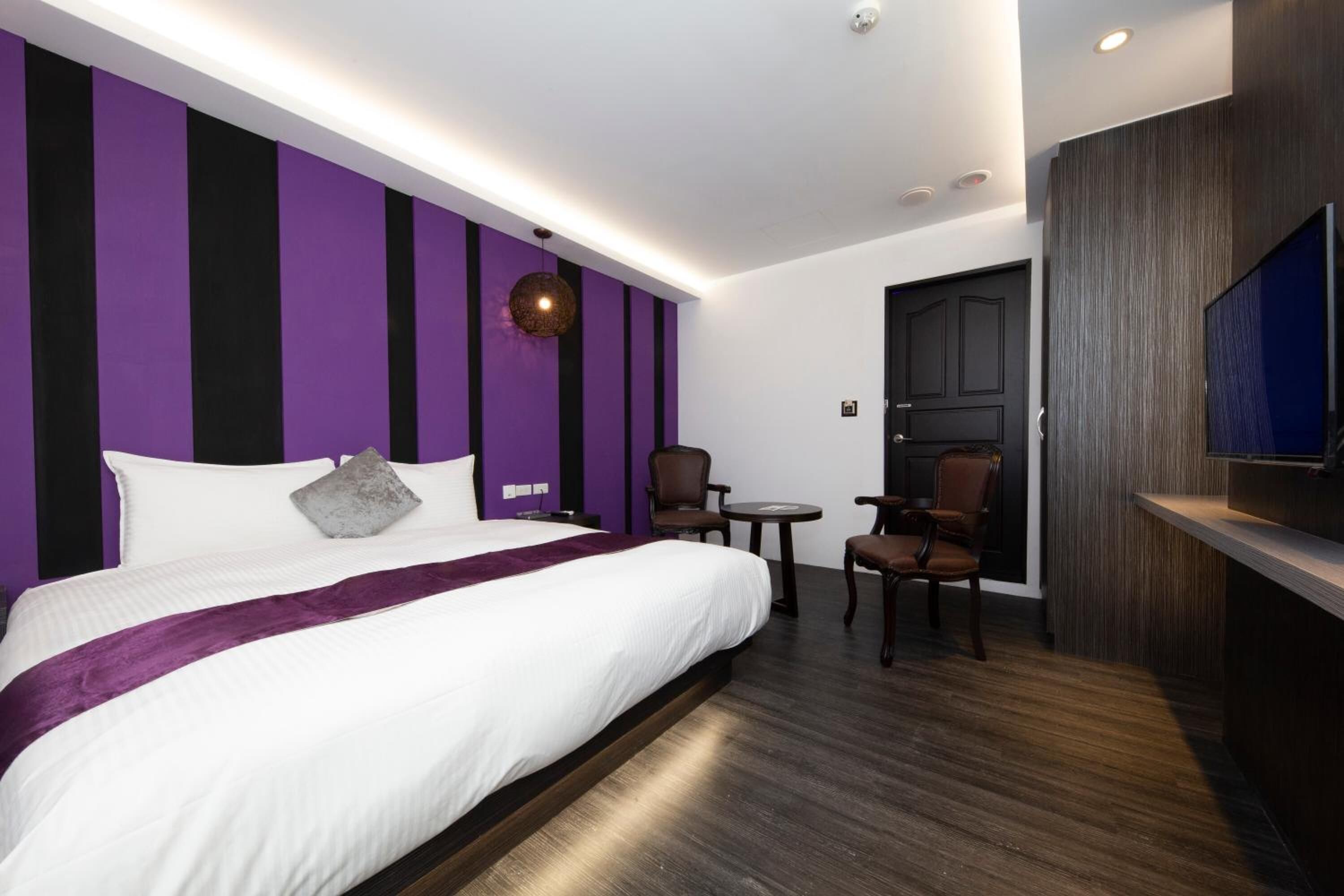 Una habitación de hotel moderna con una cama grande, un televisor, un escritorio y una silla.
