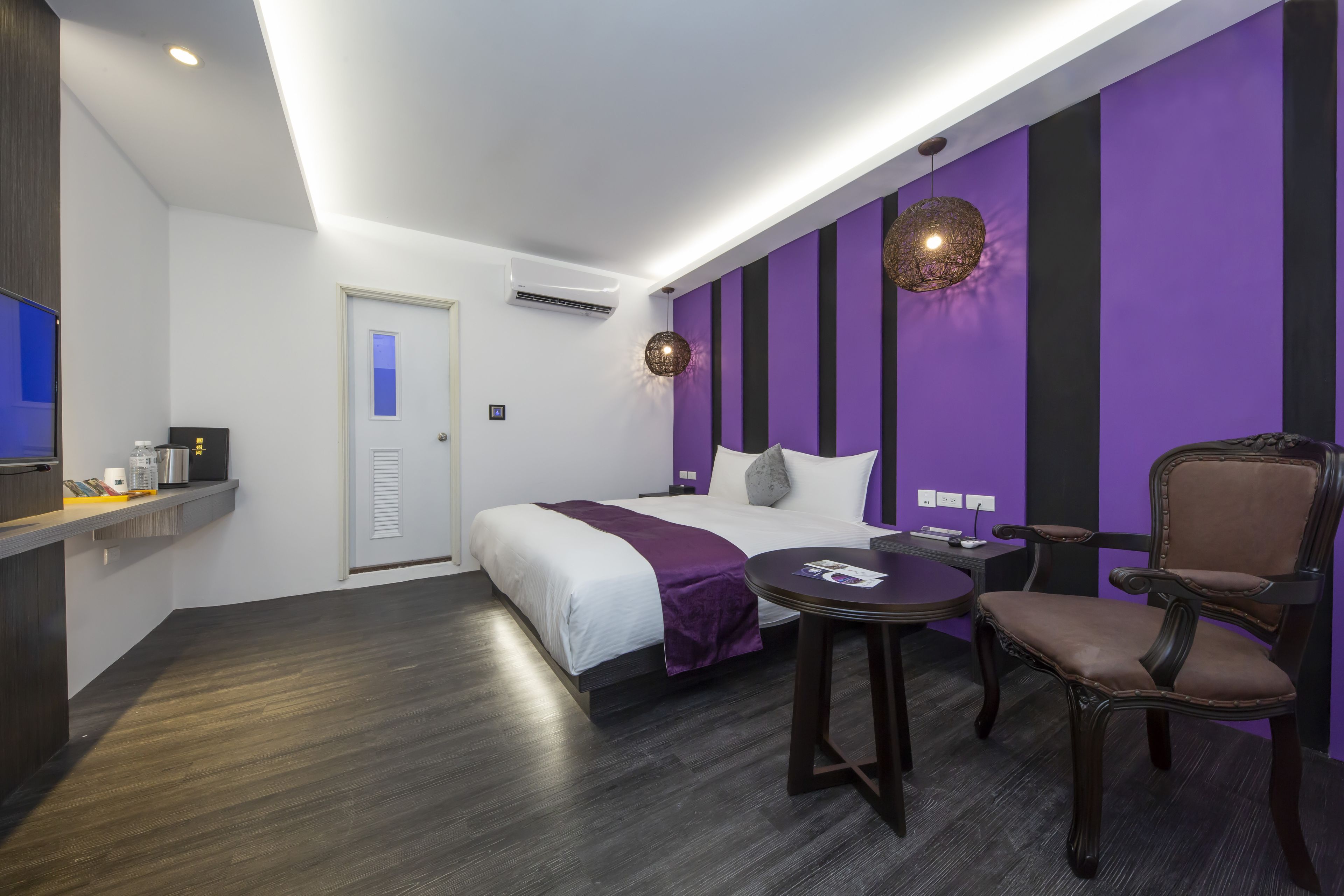 A modern hotel room with a bed, a desk, a chair, and a small table.