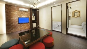 A modern hotel room with a brick wall, a flat-screen TV, a glass table, red cushioned seating, a chandelier, a large mirror, and a sliding door leading to a bedroom. - Fukun 3 Motel (Yilan)