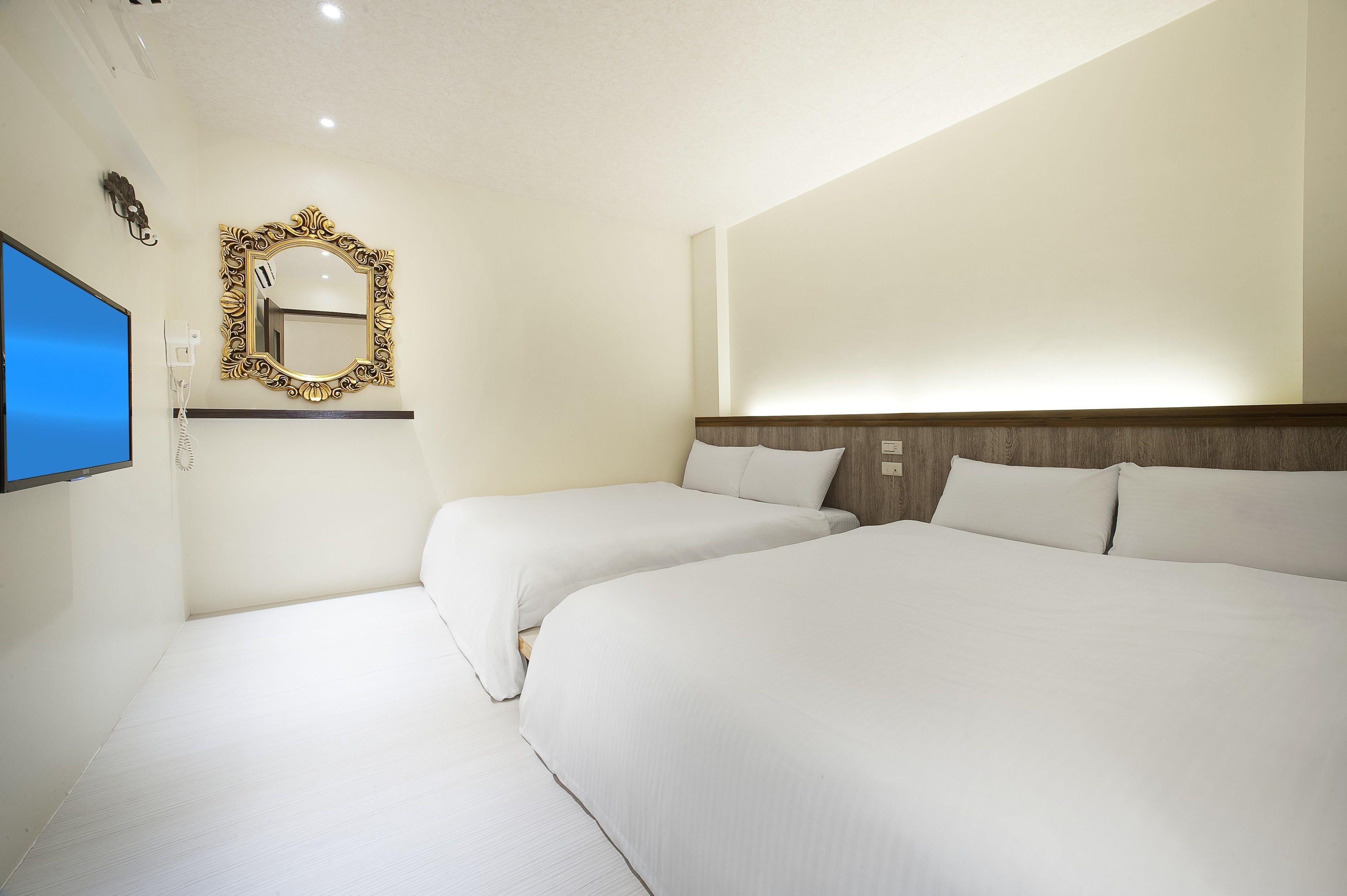 Habitación de hotel con dos camas, un espejo grande, un televisor de pantalla plana y un teléfono instalado en la pared.