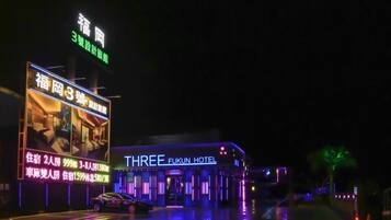 A hotel named 'THREE FUKUN HOTEL' with illuminated signage and a large billboard advertising rooms and prices.