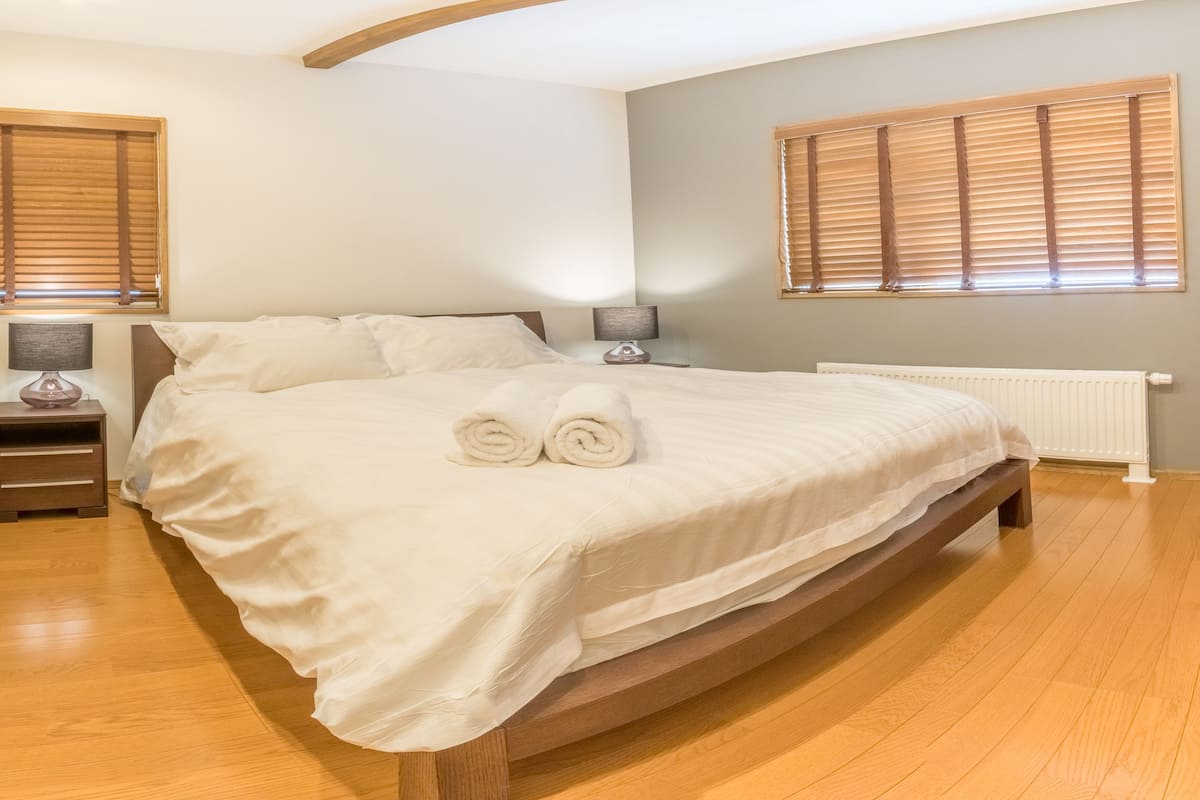 A bedroom with a large bed, two bedside tables, a nightstand, and a window with blinds.