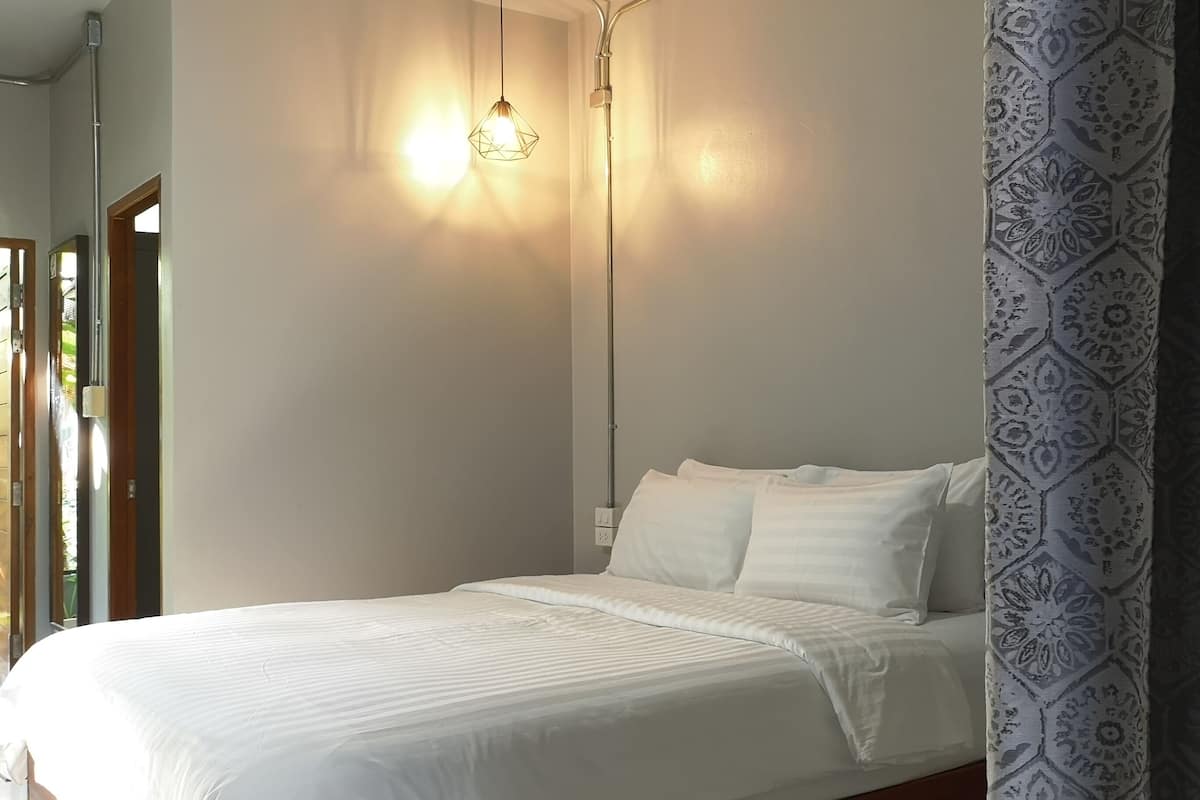 Un dormitorio con cama, ropa de cama blanca, lámpara colgante y papel tapiz estampado.